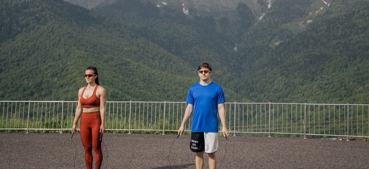Two adults skipping rope outdoors with mountains in the background, showcasing fitness and nature.