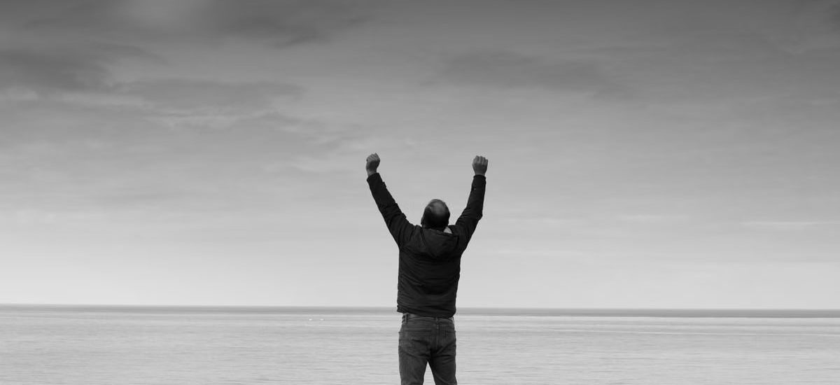 Black and white image of a person raising arms in celebration by the sea.